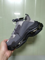 Side and outsole view of the gray and black Balenciaga Triple S sneaker held in hand.