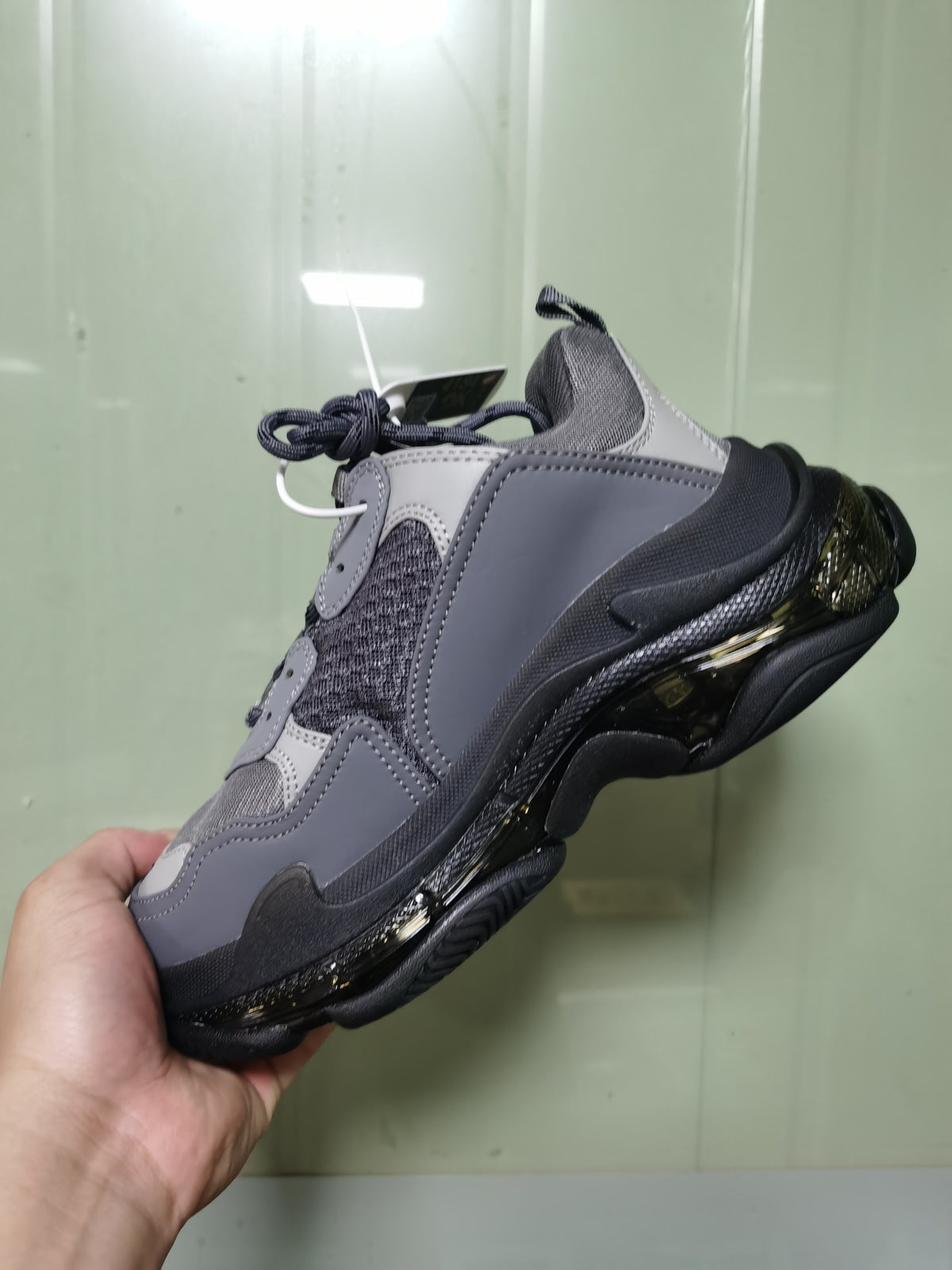 Side and outsole view of the gray and black Balenciaga Triple S sneaker held in hand.