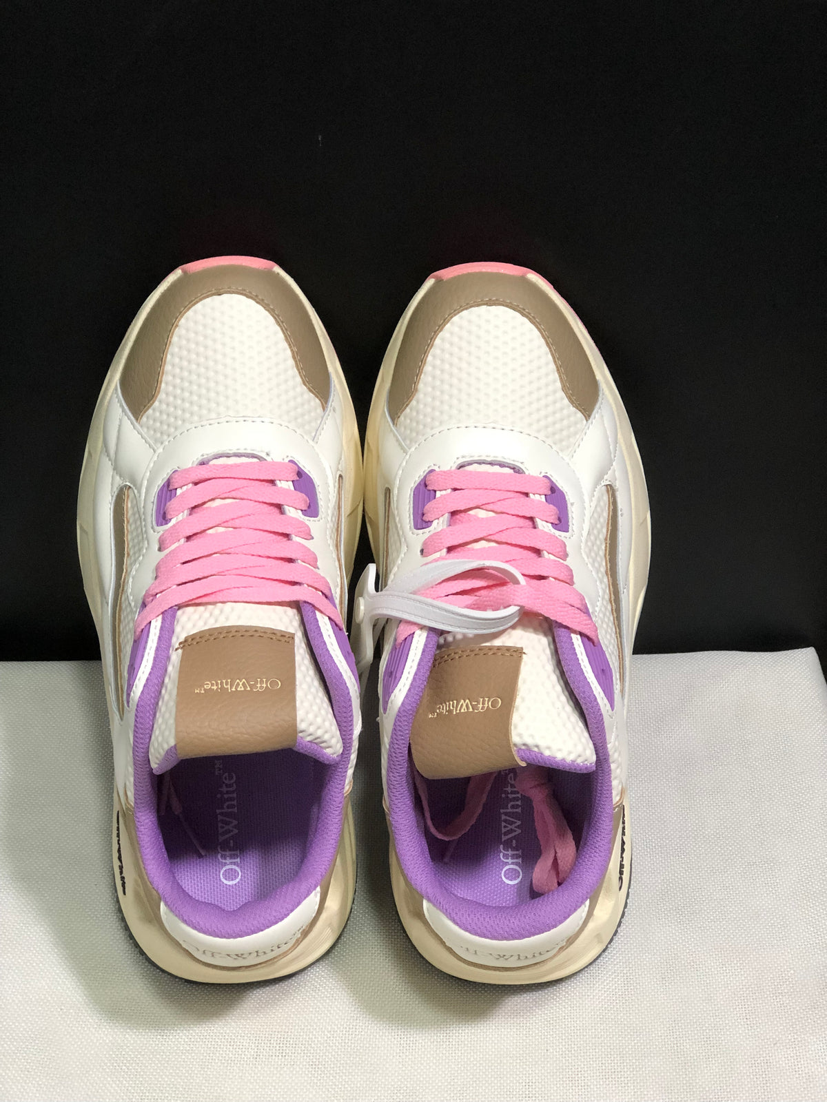 Top-down view showing the pink laces, purple eyelet panels, textured white uppers, and beige tongue accents.