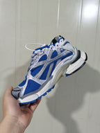 Close-up side view of a white and blue Balenciaga Runner sneaker showing mesh panels, layered overlays, and a clear heel section.
