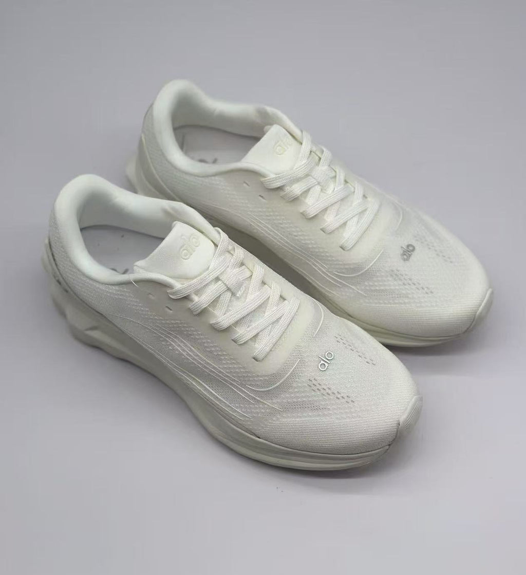 Top three-quarter view of a pair of white Alo sneakers with tonal laces and branding.