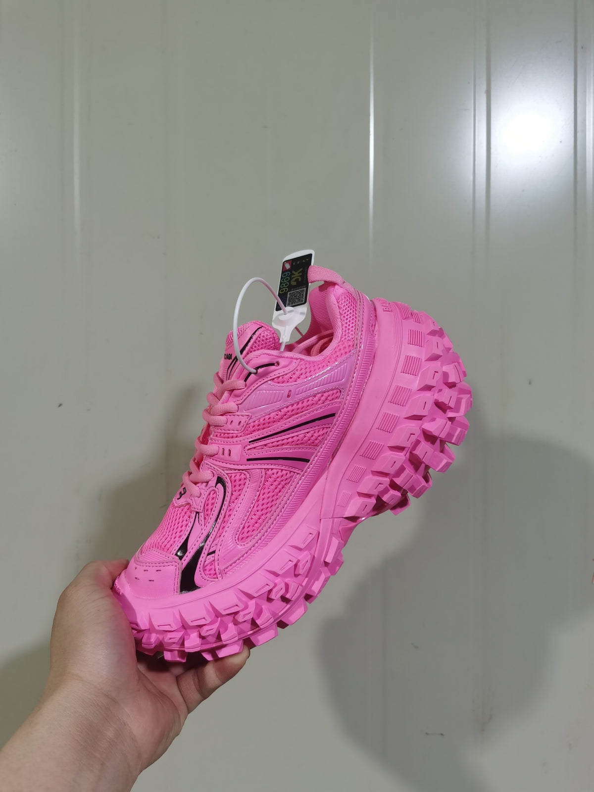 Angled view of the bright pink sneaker showing the lace area, layered side panels, padded collar, and chunky lugged outsole.