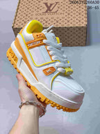Angled side view of a white Trainer Maxi sneaker with orange logo accents and a yellow lugged outsole.