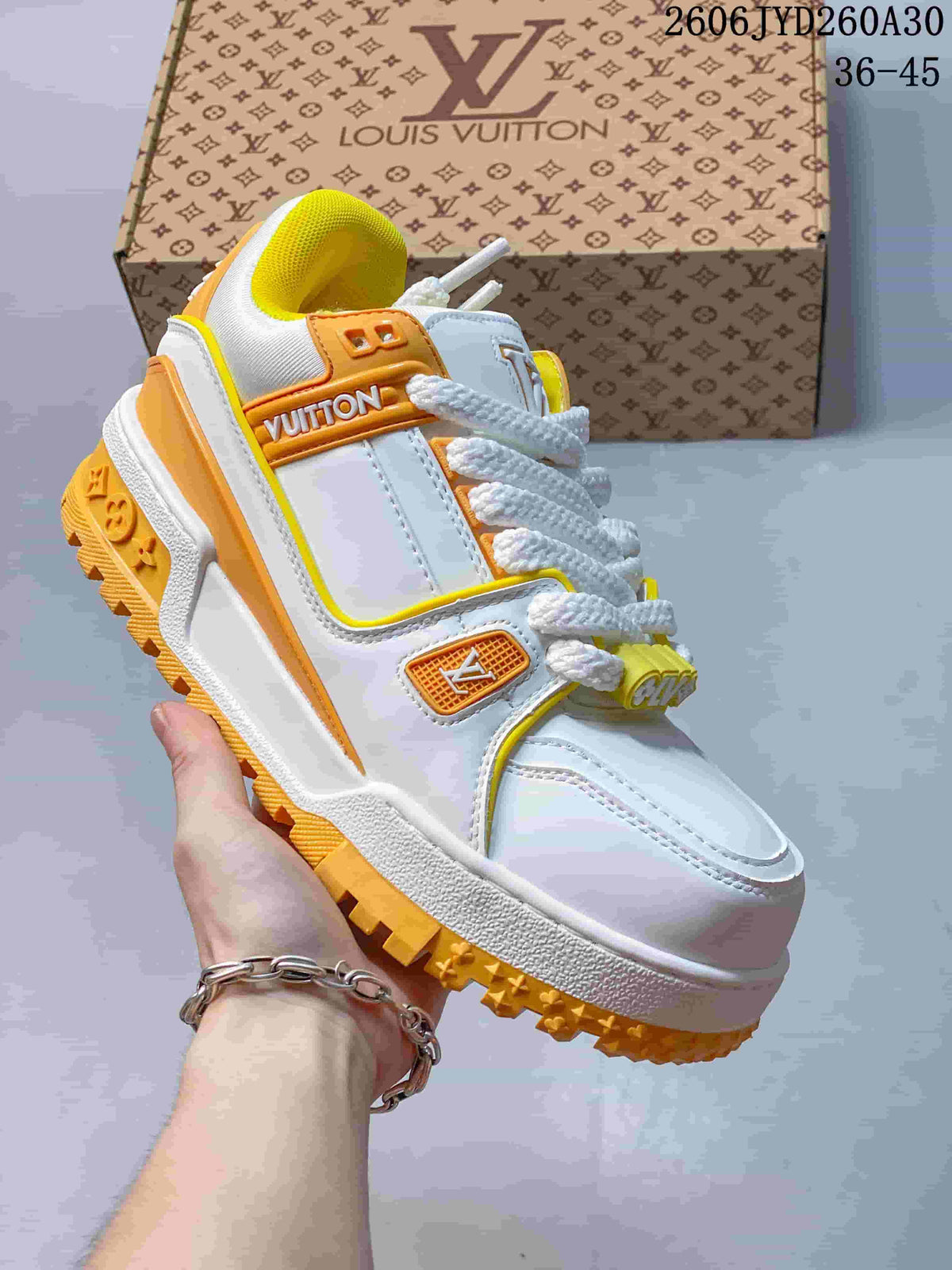 Angled side view of a white Trainer Maxi sneaker with orange logo accents and a yellow lugged outsole.