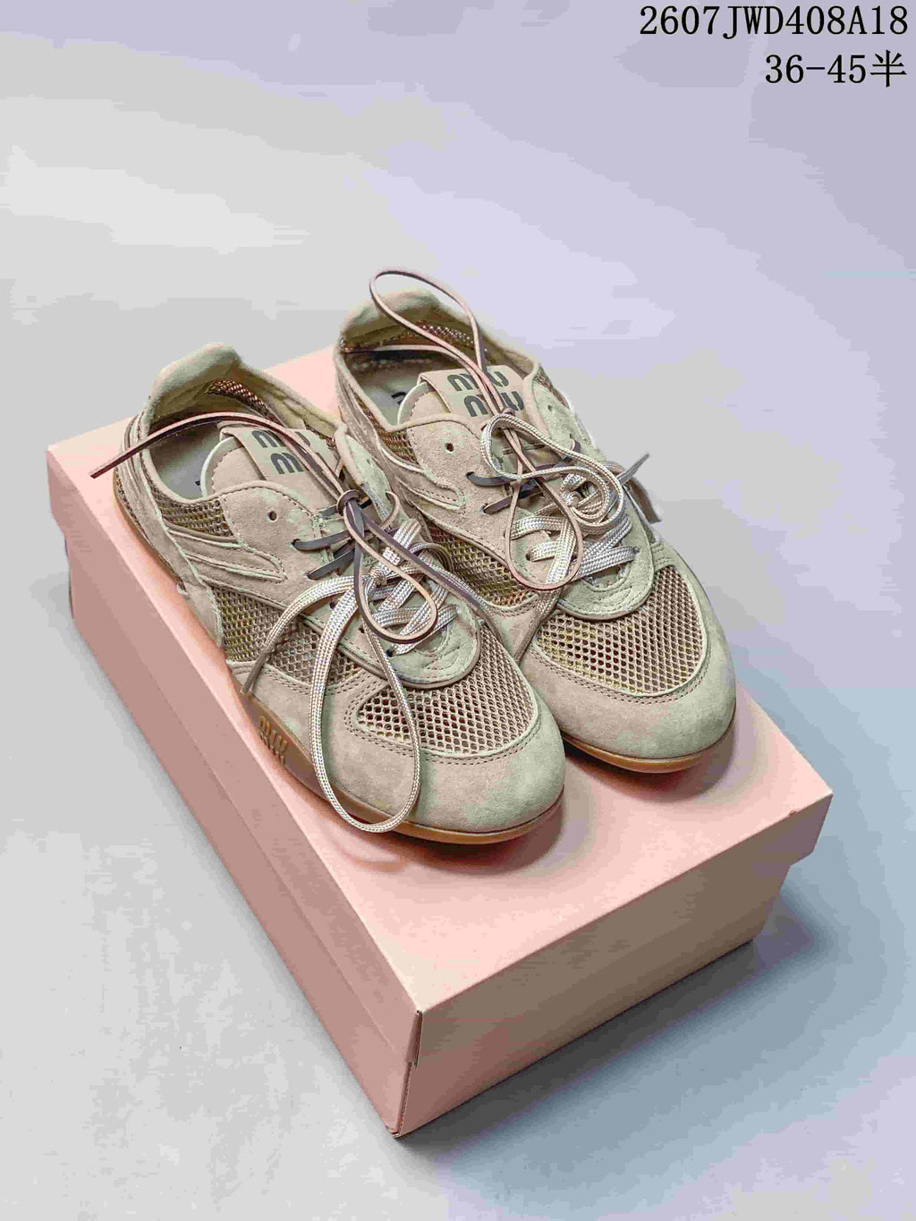 Pair of beige-sage Miu Miu Gymnasium low-top sneakers displayed on a pink shoebox, showing suede-like panels, mesh sections, laces, and rounded toes.