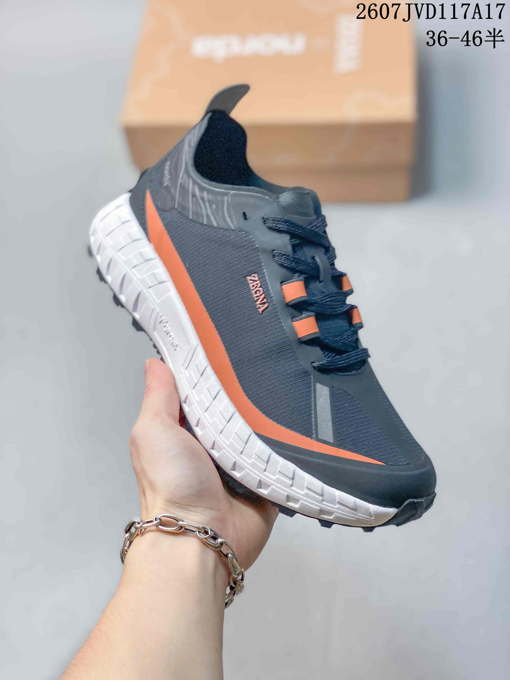 Side view of the sneaker showing the dark upper, orange side accent, white midsole, and rugged outsole.