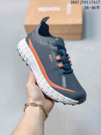 Side view of the sneaker showing the dark upper, orange side accent, white midsole, and rugged outsole.