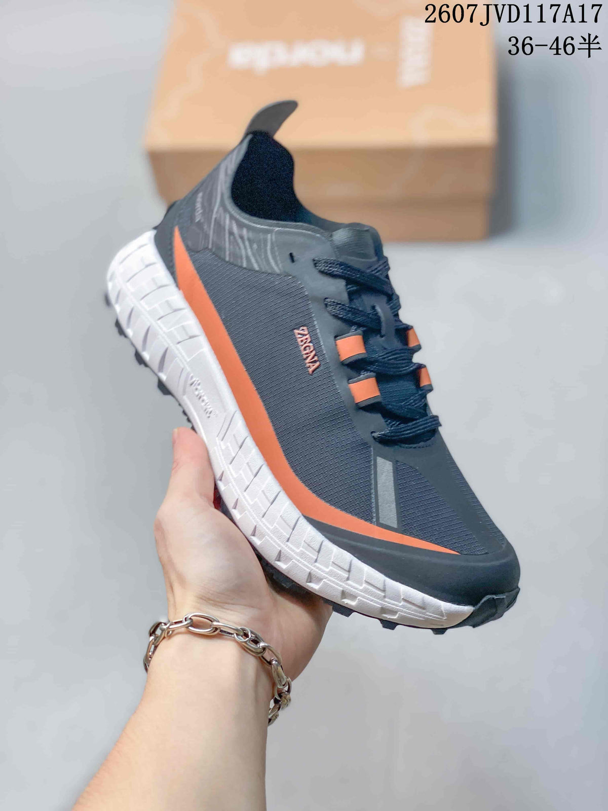 Side view of the sneaker showing the dark upper, orange side accent, white midsole, and rugged outsole.