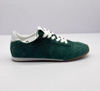 Side profile of a green Alo sneaker showing stitched panels, white heel detail, and a brown outsole.