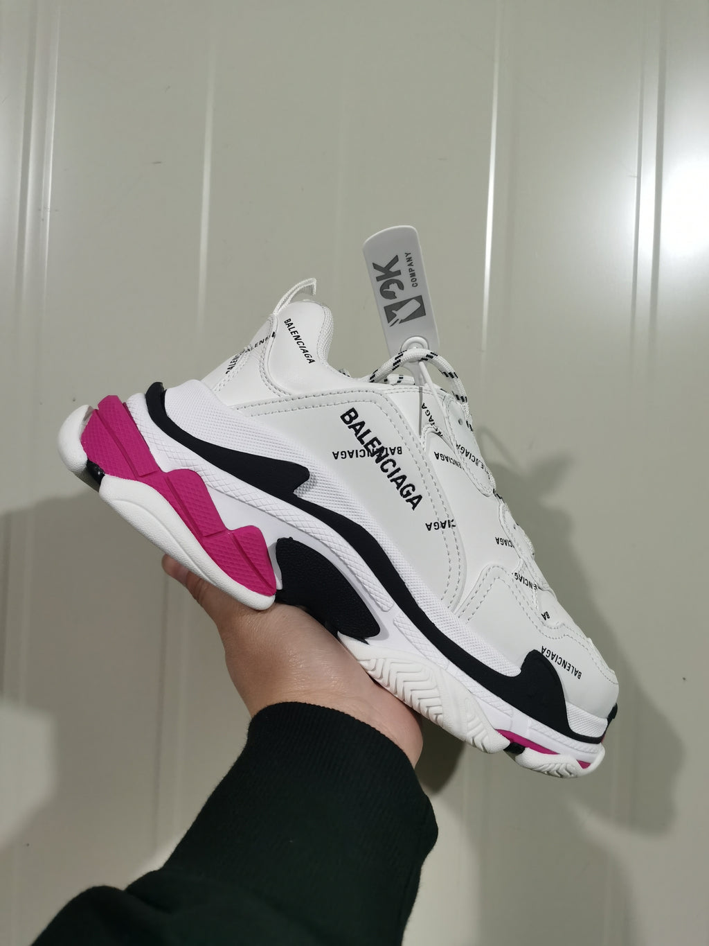Angled view of a white Balenciaga Triple S sneaker showing repeated branding, black side details, and pink sole accents.