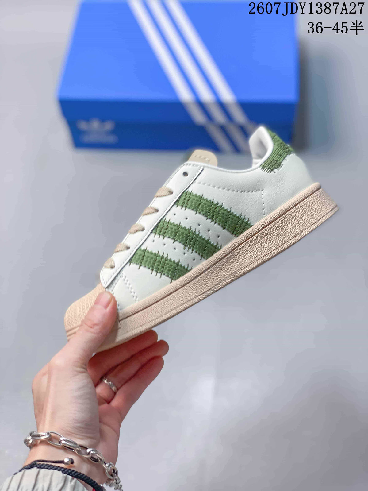 Side view of the sneaker showing the white upper, green striped detailing, beige sole, and low-top profile.