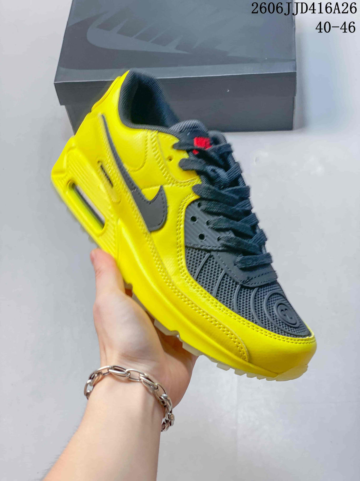 Angled side view of the yellow and black Nike Air Max 90 sneaker showing the Swoosh, layered upper, and heel window.