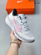 Close-up of a light gray and white Nike Quest 6 sneaker with pink side detailing and a perforated upper.
