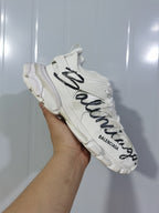 Side view of a white Balenciaga Track sneaker highlighting the black graffiti-style lettering and layered upper.