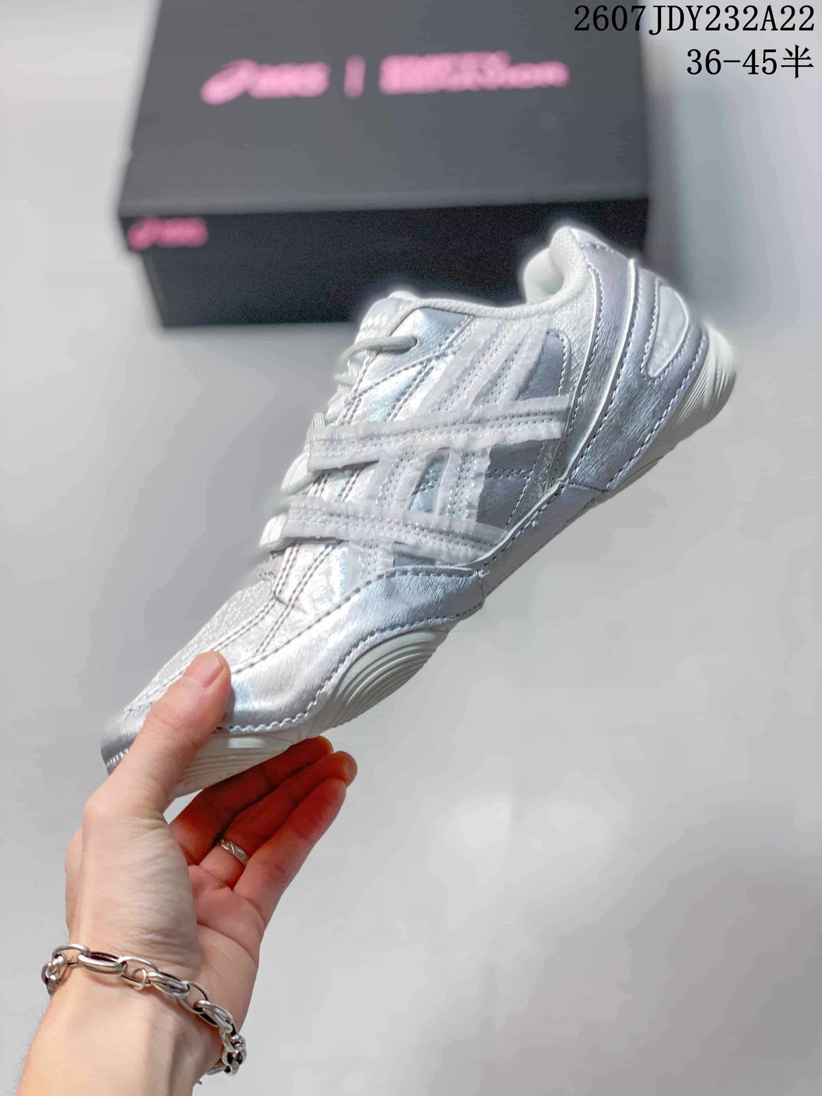 Side view of the low-top silver and white sneaker highlighting layered panels, lace-up construction, and a low-profile sole.