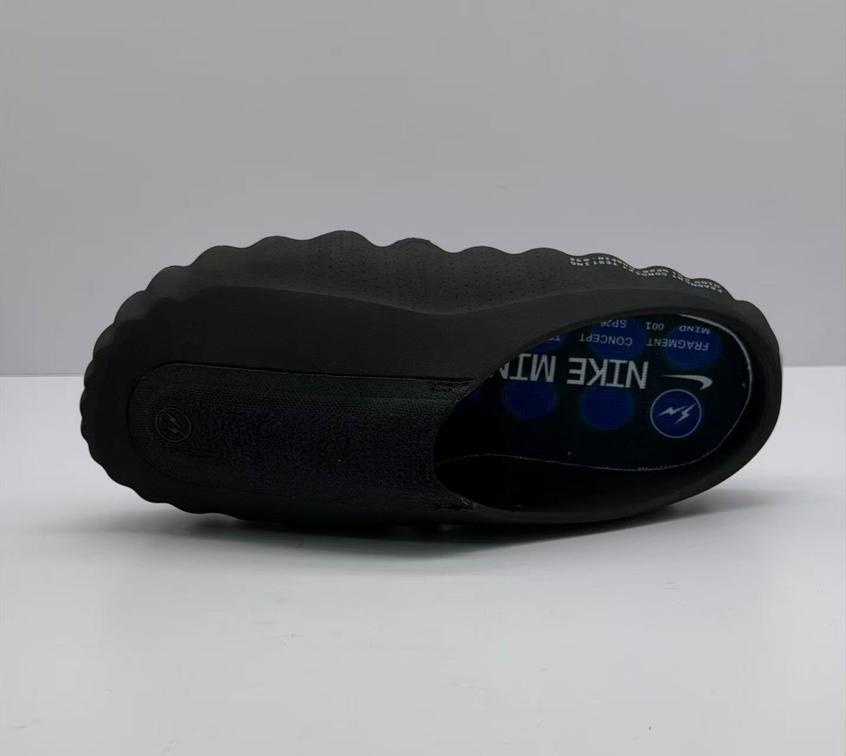 Bottom-side view of one black slide sandal showing its sculpted profile and printed footbed.