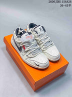 Pair of white low-top sneakers with monogram panels, layered rope laces, dark overlays, and an orange branded shoebox.