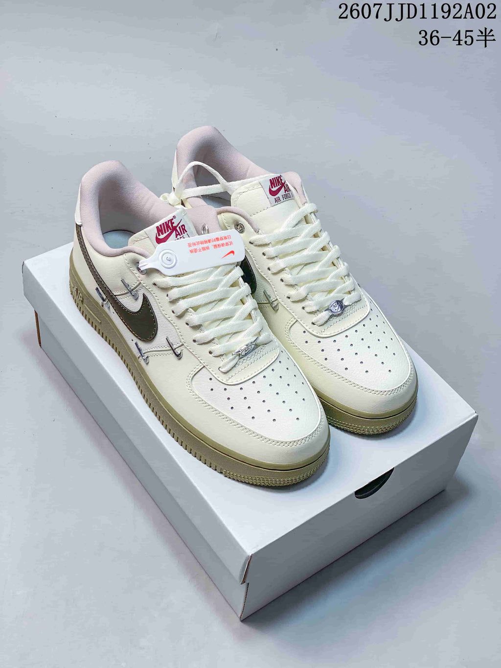Pair of cream low-top sneakers with dark gray Swoosh details, perforated toes and pale olive-colored outsoles.