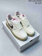 Pair of cream low-top sneakers with dark gray Swoosh details, perforated toes and pale olive-colored outsoles.