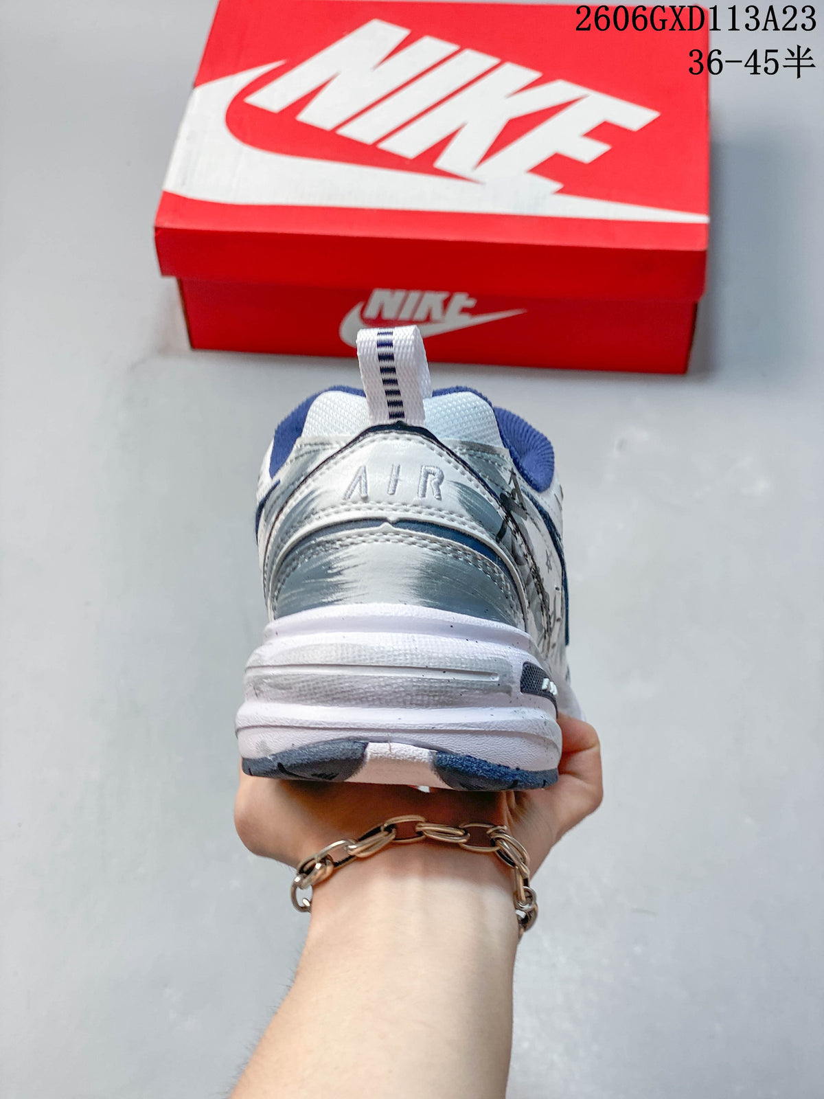 Rear view of a white Nike Air Monarch IV sneaker with silver heel detailing and navy lining.