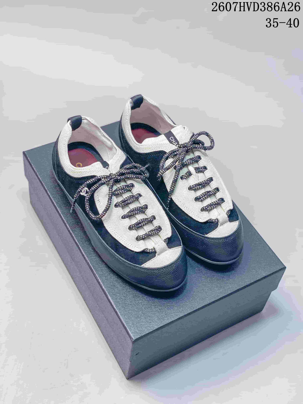 Pair of black-and-white low-top Chanel trainers displayed on a box, showing the rounded toe and contrasting laces.