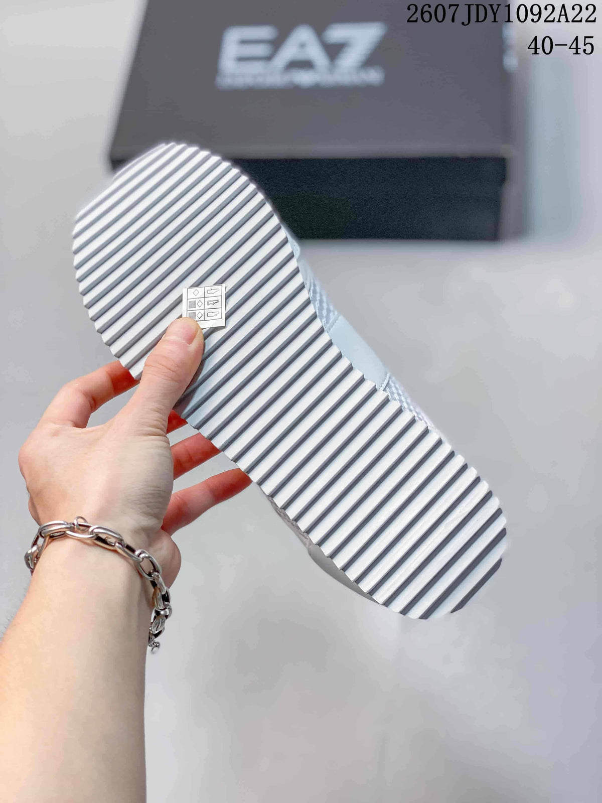 Close view of the white sneaker outsole showing a serrated linear tread pattern; source overlay shows style code 2607JDY1092A22 and size range 40–45.