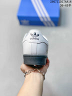 Rear view of a white Superstar sneaker with adidas branding on the heel and a black outsole.