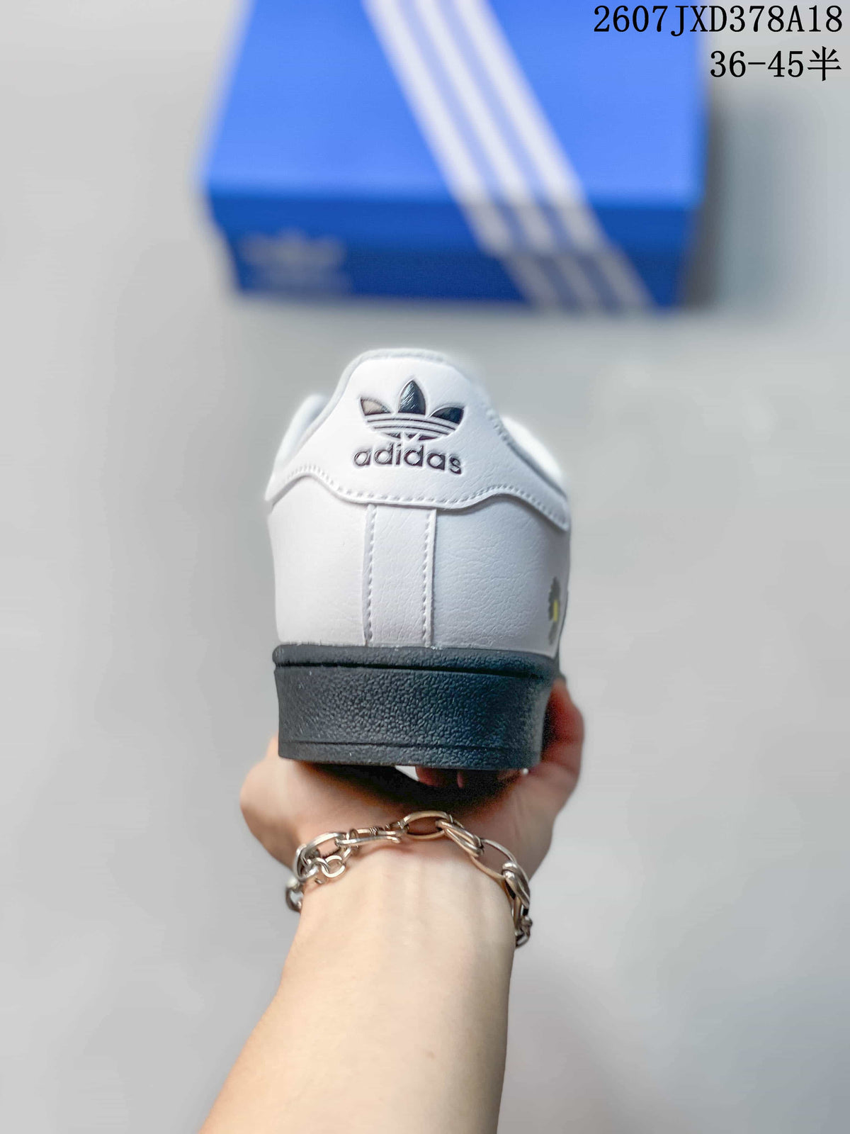 Rear view of a white Superstar sneaker with adidas branding on the heel and a black outsole.
