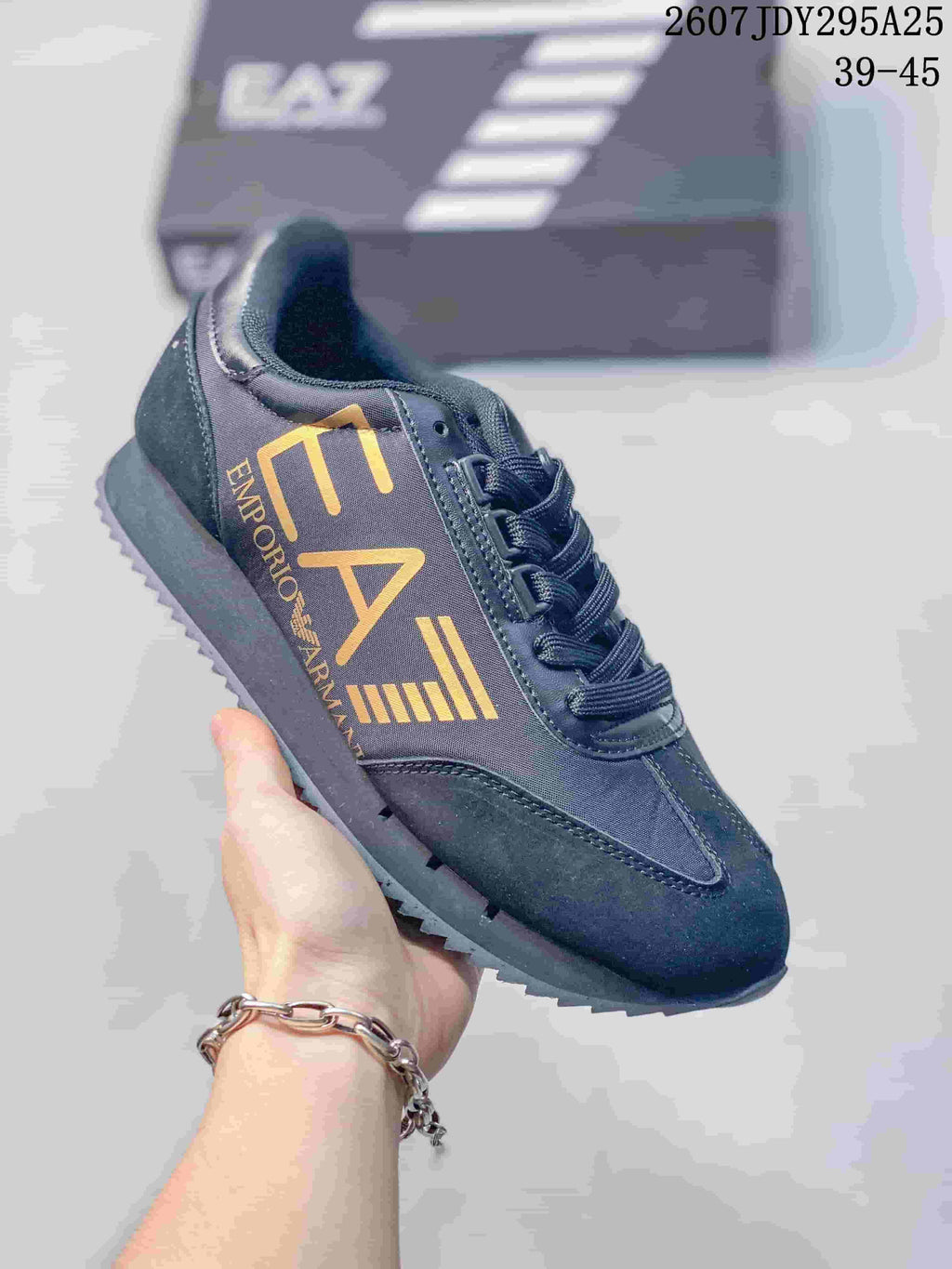 Close-up of a black Emporio Armani EA7 sneaker with gold side branding, black laces and a dark textured outsole.