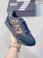Close-up of a black Emporio Armani EA7 sneaker with gold side branding, black laces and a dark textured outsole.