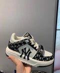 Black and white MLB M001 sneaker held in hand, showing New York Yankees graphics, a repeating monogram-style upper pattern, white laces, and a layered outsole.