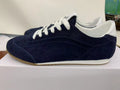 Side view of a deep blue low-top sneaker with white laces, white collar detailing, and a gum-colored outsole.