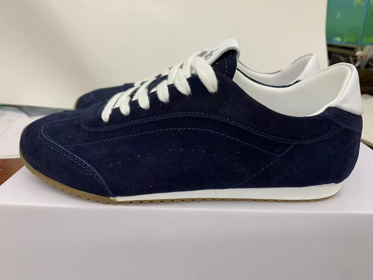 Side view of a deep blue low-top sneaker with white laces, white collar detailing, and a gum-colored outsole.