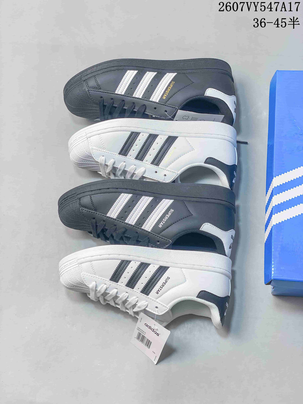White and black Superstar sneakers arranged together beside a blue adidas shoebox.