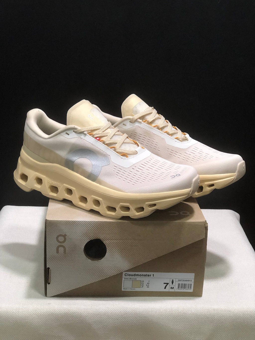 Pair of On Cloudmonster 1 sneakers in a light cream and white colorway displayed on the labeled shoe box.
