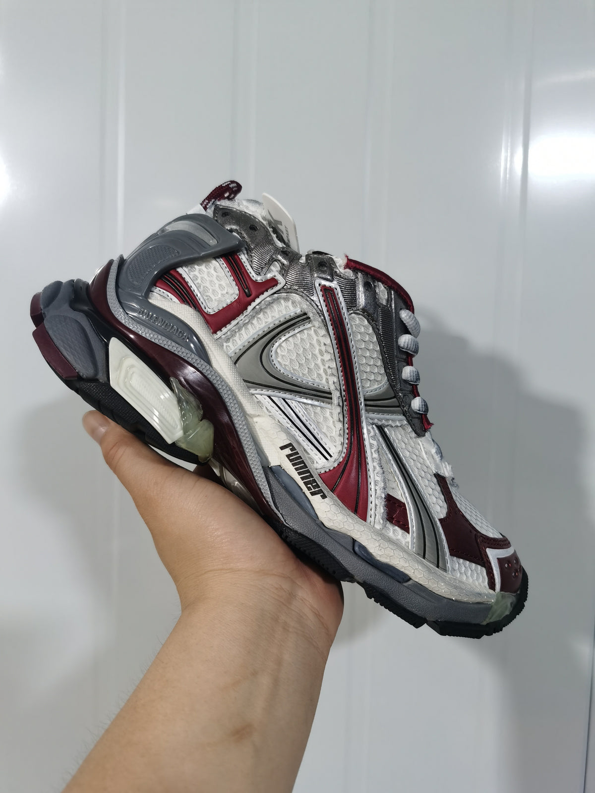 Close-up three-quarter view of Puma Runner sneakers in metallic white, gray, and wine red.