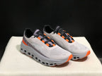 Angled view of the gray On Cloud X pair with orange details and open sections in the sole.
