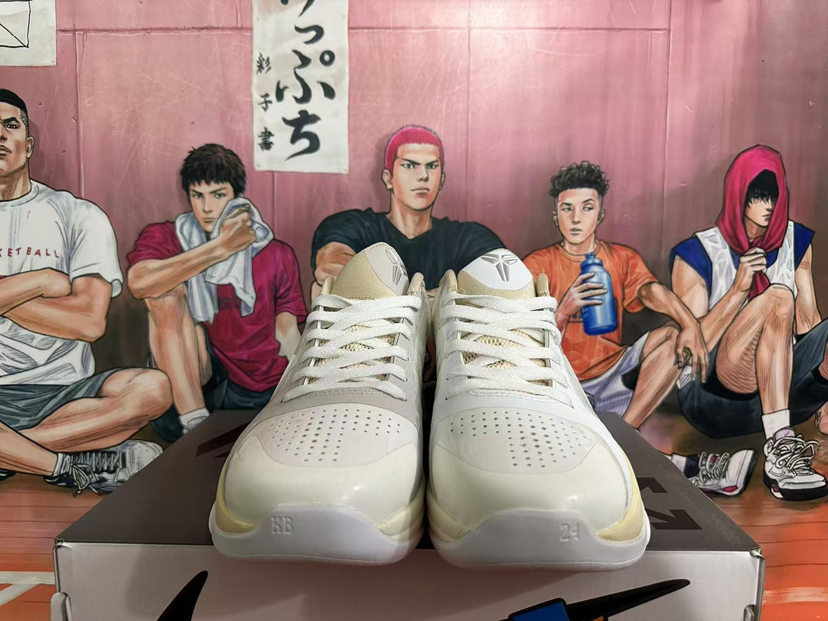 Front view of pale cream low-top basketball shoes with white laces, perforated toe panels, and Kobe logos on the tongues.