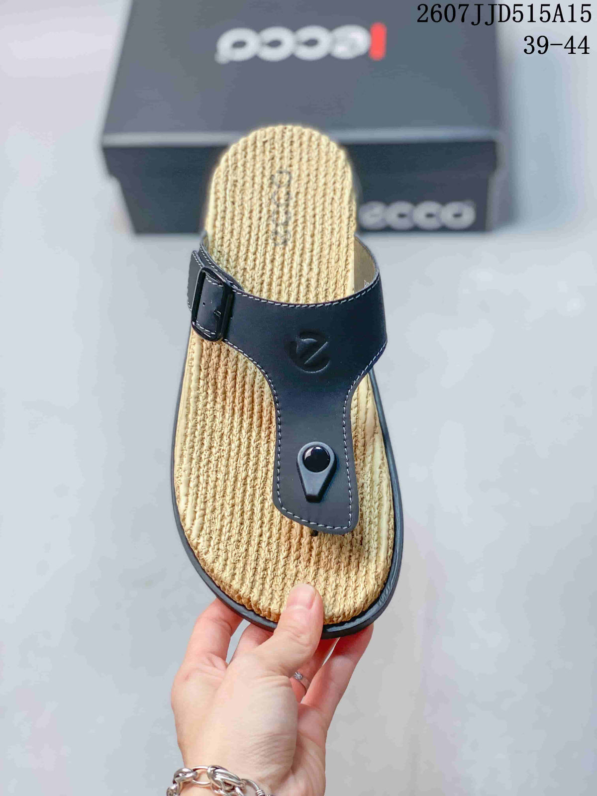 Top view of one black thong sandal with a tan textured footbed, buckle strap, and central toe post.