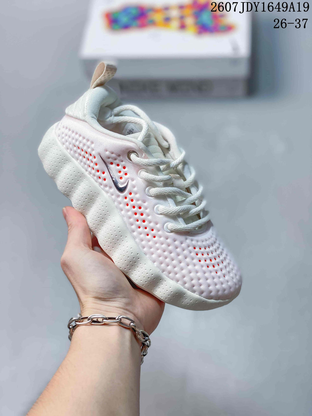 White Nike Mind 002 kids sneaker with red-orange accents visible through the perforations.