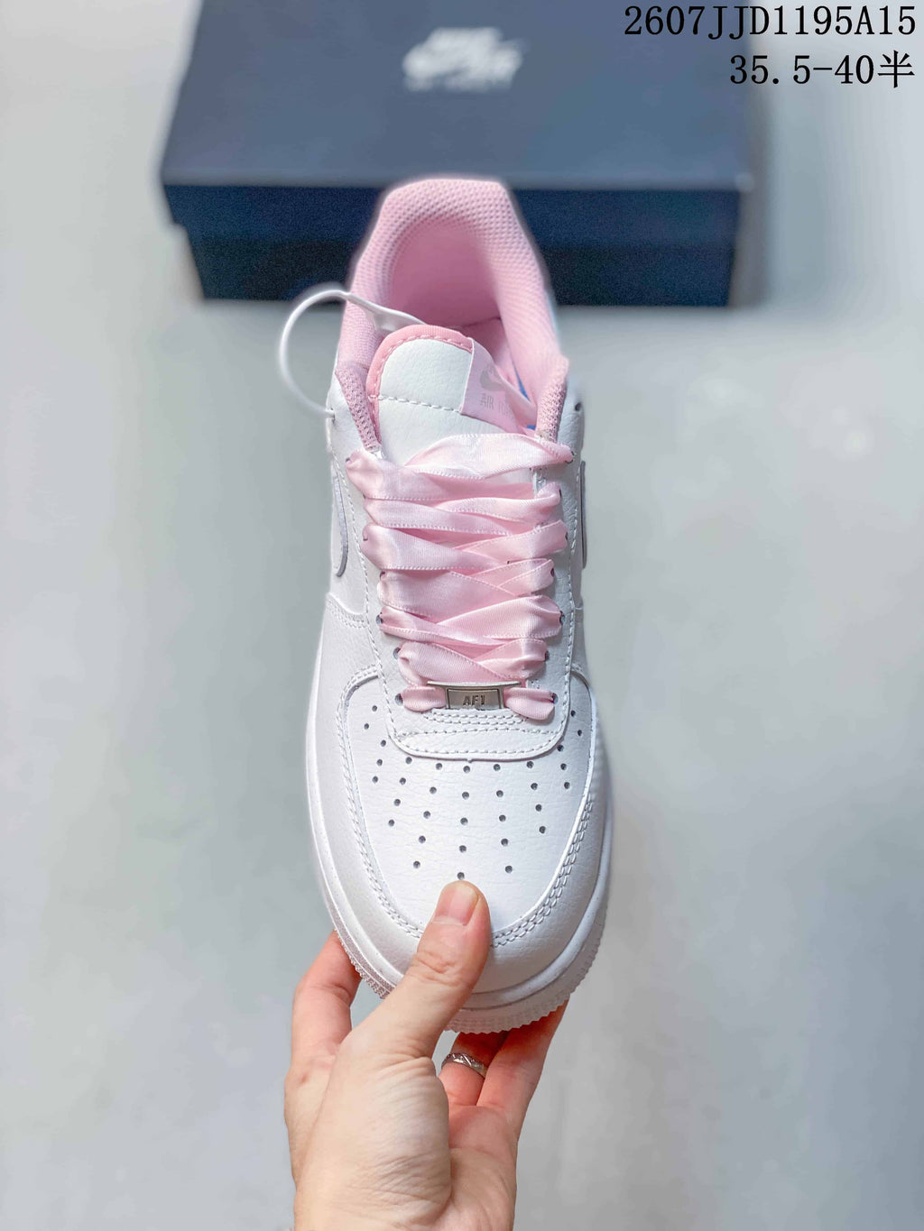 Top view of a white sneaker with pink satin-style laces, pink tongue and collar details, and a perforated toe box.
