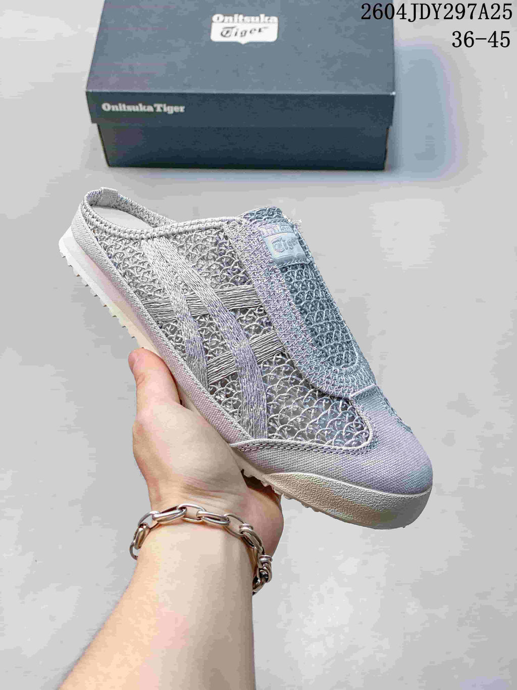 Light gray Onitsuka Tiger Mexico 66 Sabot sneaker held in hand with its box behind it; the image shows style code 2604JDY297A25 and size range 36–45.
