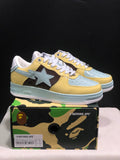 Pair of BAPE STA low-top sneakers in yellow, light blue, brown, and white, displayed above a branded shoebox.