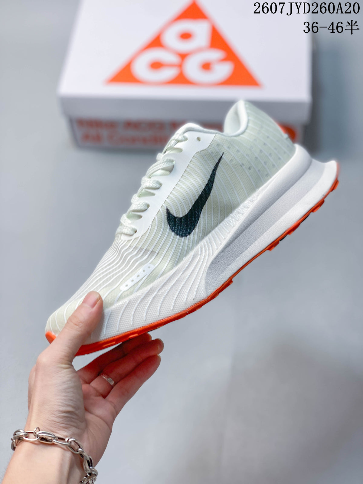 Side profile of an off-white Nike ACG Ultrafly Trail sneaker with black side branding and an orange outsole edge.