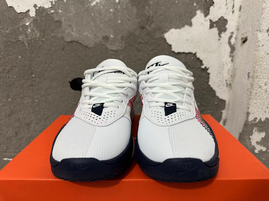 Front view of white Nike basketball shoes with black toe accents, white laces, and red side details.