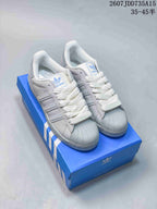Pair of white and gray adidas Superstar sneakers displayed on a blue shoebox, showing the shell toes and blue branding.