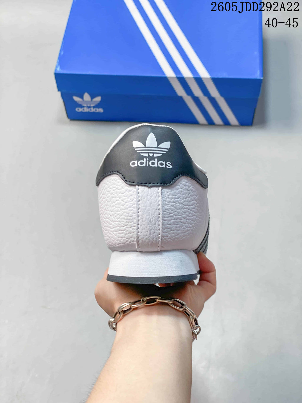 Rear view of the white sneaker showing the dark heel panel, adidas branding, and blue shoe box.