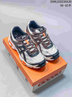 Pair of ASICS GEL-CUMULUS 16 shoes displayed on an orange shoebox, showing light uppers, dark overlays and orange accents.