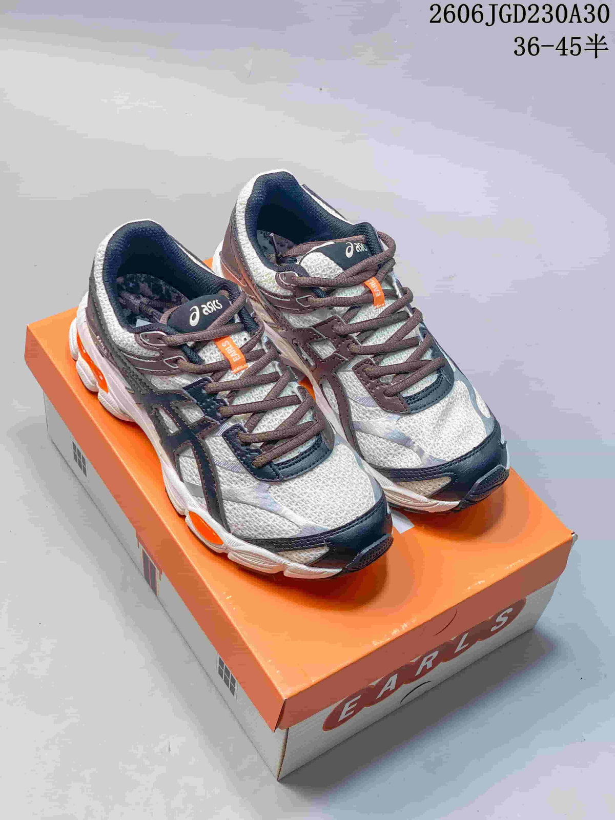 Pair of ASICS GEL-CUMULUS 16 shoes displayed on an orange shoebox, showing light uppers, dark overlays and orange accents.