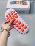 Underside of a light pink slide showing rows of raised orange outsole pods.